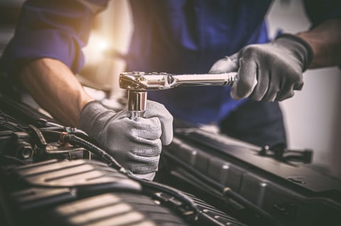 Técnico automotriz revisando el motor de un auto con herramienta